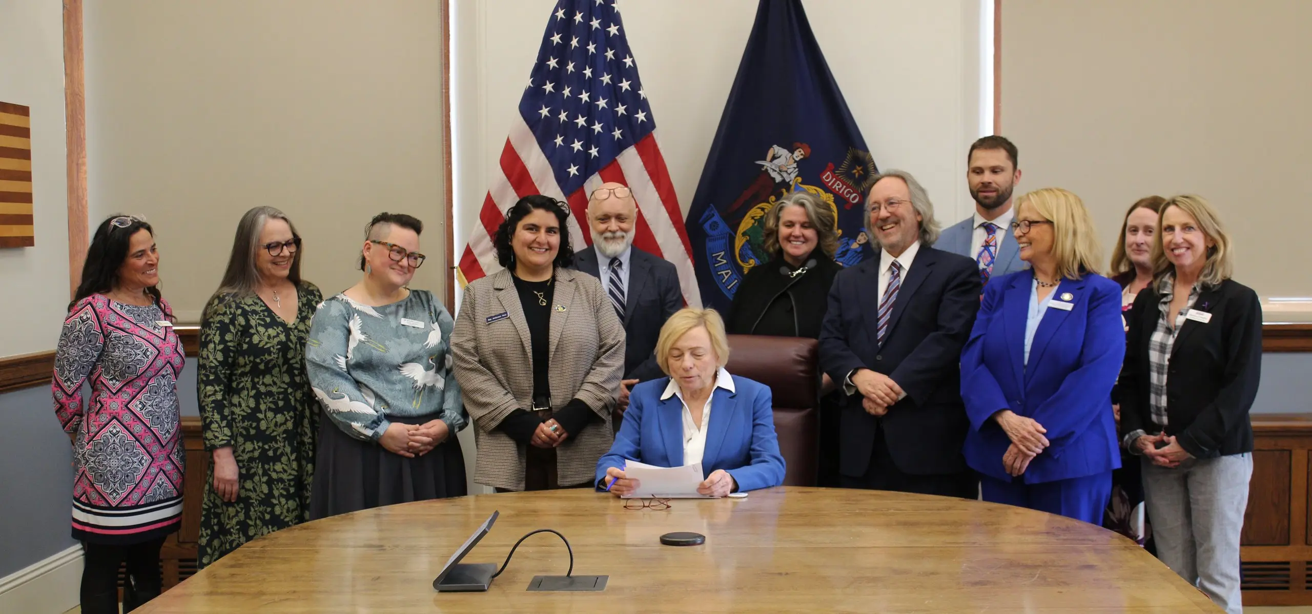 Advocates and legislators gathered around a bill signing in front of the American and Maine flags